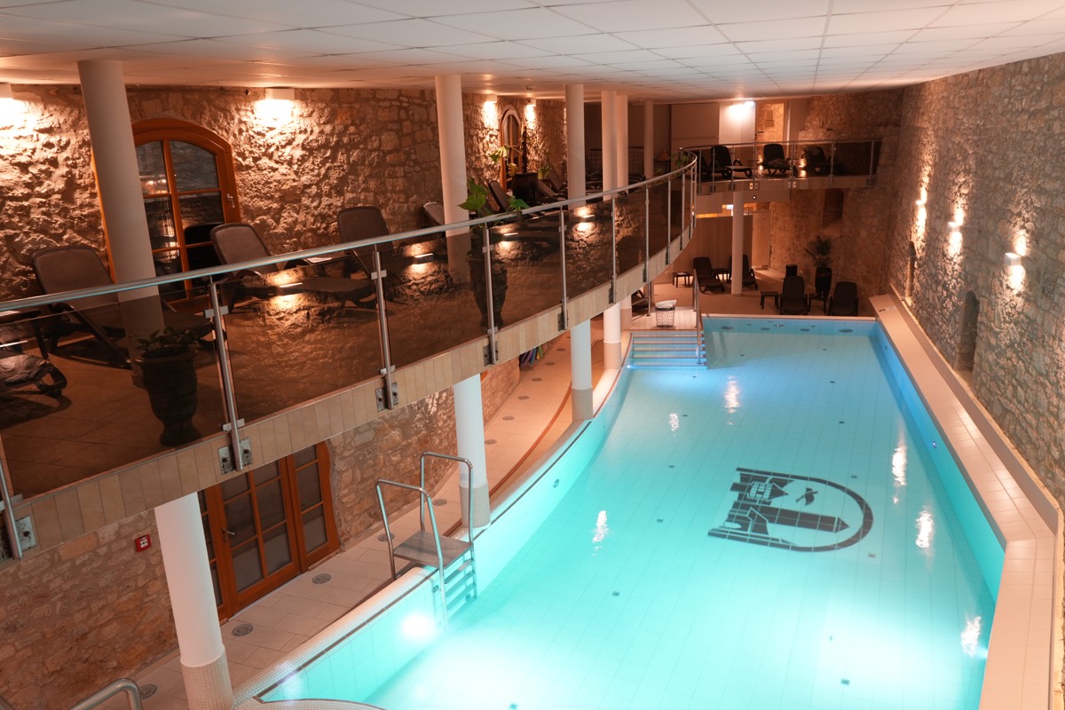 Beleuchtetes Hallenbad im Wasserschloss Westerburg am Abend, Galerie mit Ruheliegen über dem Becken